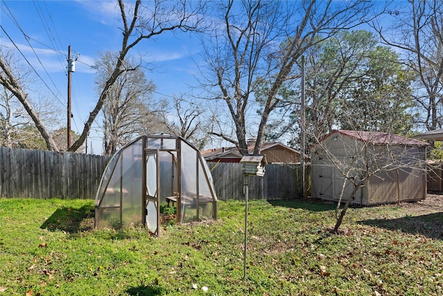 view of yard featuring a fenced backyard, a greenhouse, and an outbuilding