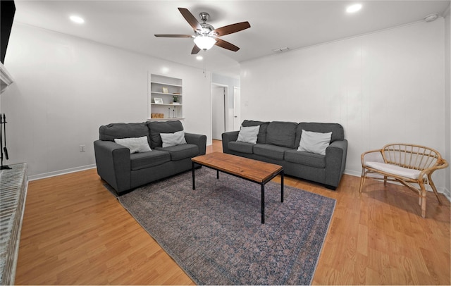 living area with built in features, visible vents, light wood-style flooring, a ceiling fan, and baseboards