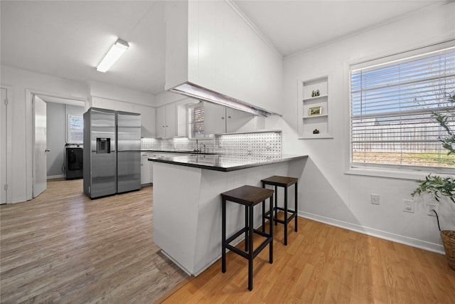 kitchen featuring light wood finished floors, dark countertops, a peninsula, stainless steel refrigerator with ice dispenser, and a sink