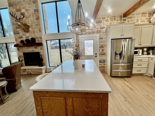 kitchen with white microwave, light wood-style flooring, a fireplace, stainless steel refrigerator with ice dispenser, and beam ceiling