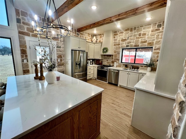 kitchen with light wood-style flooring, a sink, stainless steel appliances, wall chimney range hood, and beam ceiling