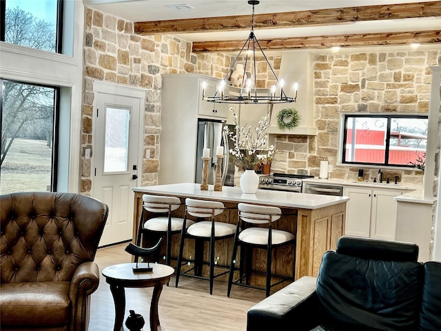 kitchen featuring stainless steel appliances, light countertops, a kitchen island, light wood-type flooring, and beamed ceiling