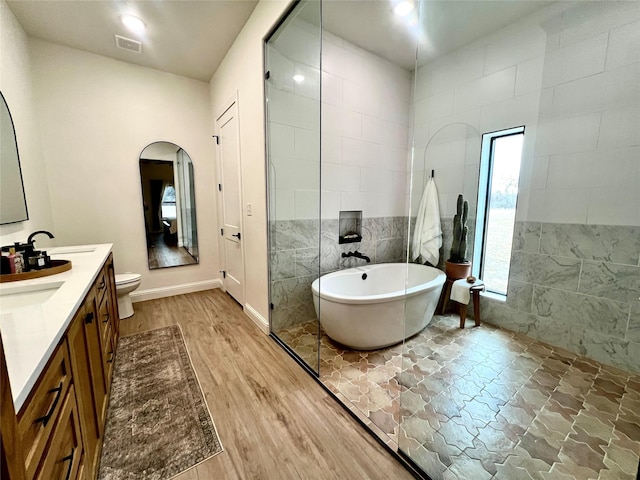 bathroom featuring tile walls, a soaking tub, visible vents, a sink, and wood finished floors