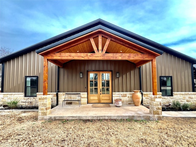 doorway to property featuring board and batten siding, stone siding, and french doors