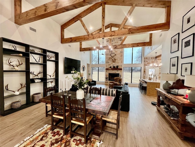 dining room featuring a notable chandelier, a fireplace, visible vents, high vaulted ceiling, and light wood-type flooring