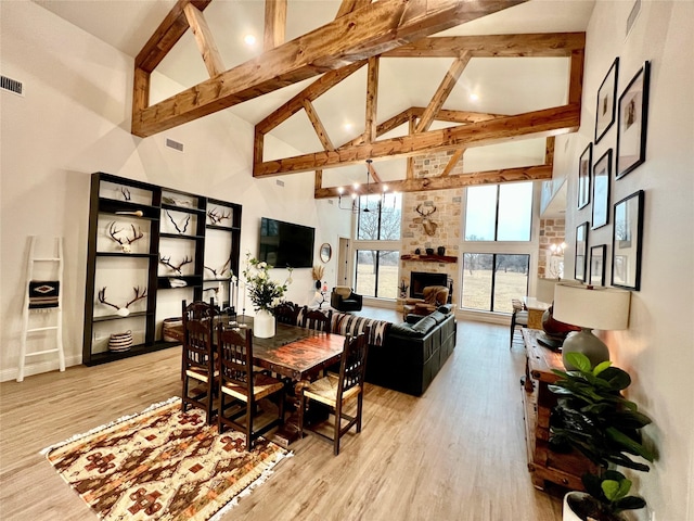 dining room with high vaulted ceiling, a stone fireplace, light wood-type flooring, and visible vents