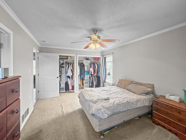 carpeted bedroom featuring visible vents, ceiling fan, ornamental molding, a textured ceiling, and two closets