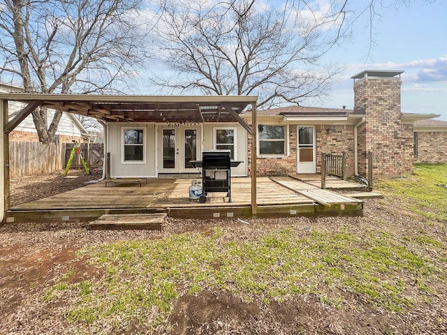 rear view of house with a deck, fence, french doors, brick siding, and a chimney