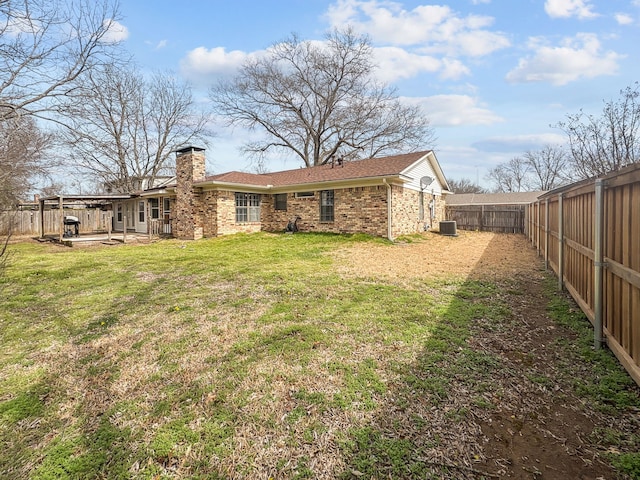 rear view of house with central AC unit, a yard, a fenced backyard, a chimney, and brick siding