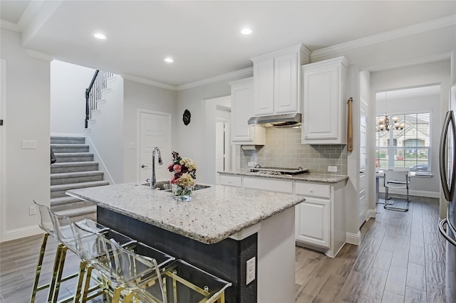 kitchen with light stone counters, crown molding, tasteful backsplash, a sink, and light wood-type flooring