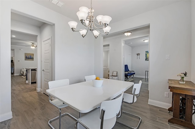 dining room with ceiling fan with notable chandelier, dark wood-type flooring, visible vents, and baseboards