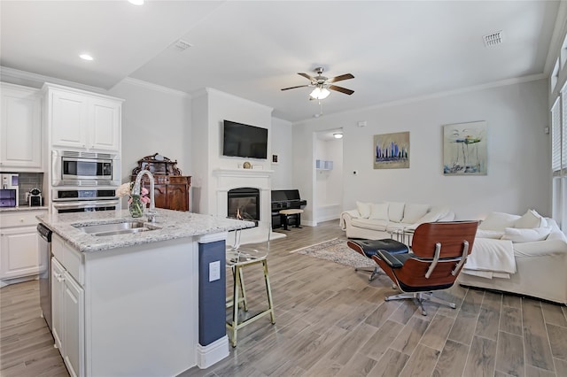 kitchen with open floor plan, stainless steel appliances, light wood finished floors, and a glass covered fireplace