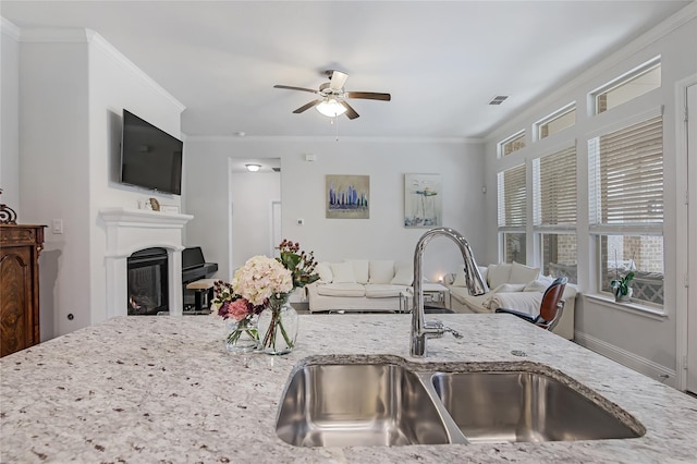 kitchen with a glass covered fireplace, light stone counters, ornamental molding, open floor plan, and a sink