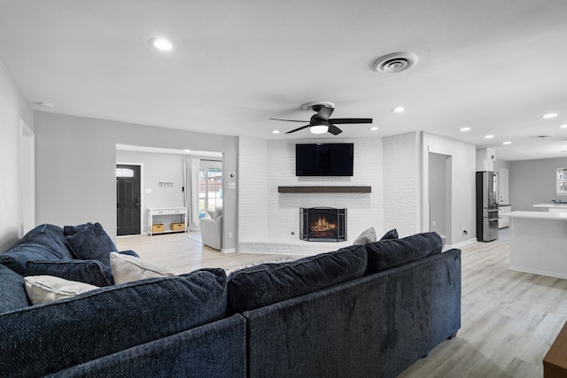 living room featuring light wood finished floors, a brick fireplace, visible vents, and recessed lighting