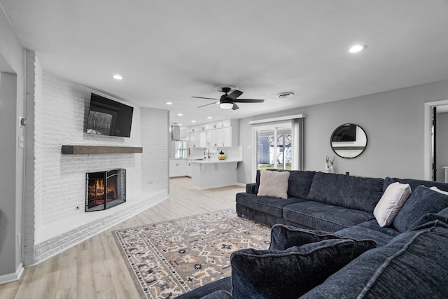 living room featuring ceiling fan, recessed lighting, a fireplace, baseboards, and light wood-style floors