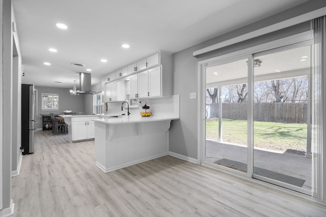 kitchen featuring a peninsula, a sink, light countertops, wall chimney range hood, and freestanding refrigerator