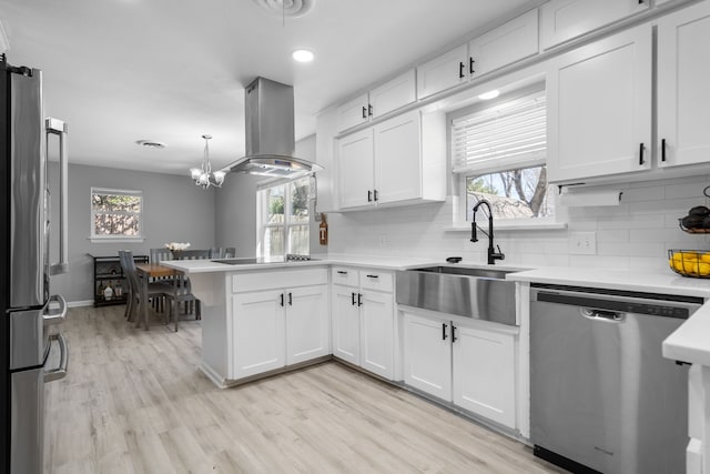 kitchen featuring stainless steel appliances, light countertops, white cabinetry, island range hood, and a peninsula