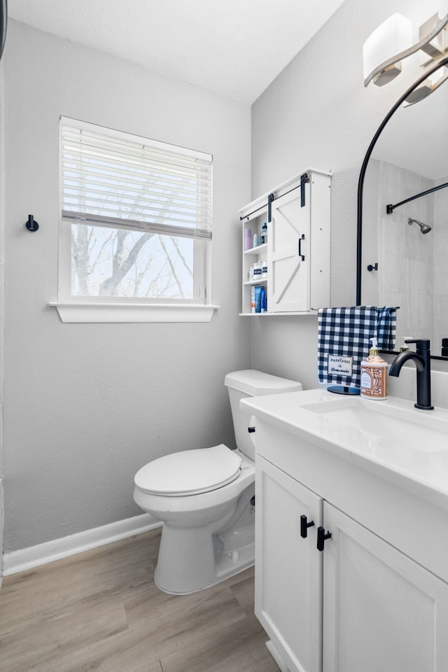 bathroom with baseboards, a shower, toilet, wood finished floors, and vanity