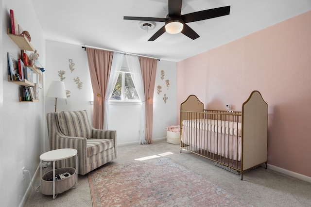 bedroom featuring a nursery area, ceiling fan, baseboards, and carpet flooring