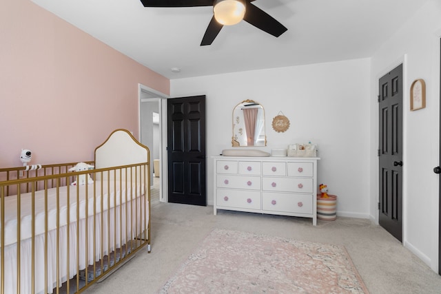 carpeted bedroom with a nursery area, ceiling fan, and baseboards