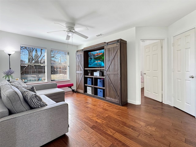 living room featuring a barn door, visible vents, baseboards, dark wood-style floors, and ceiling fan