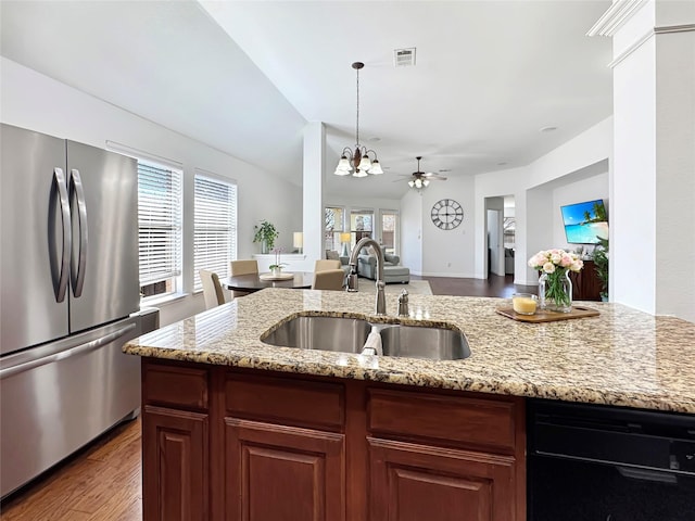 kitchen featuring visible vents, light stone counters, open floor plan, freestanding refrigerator, and a sink