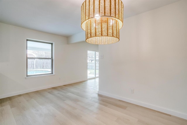 empty room featuring light wood-type flooring, plenty of natural light, and an inviting chandelier