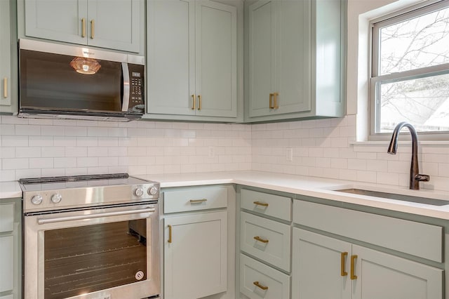 kitchen featuring appliances with stainless steel finishes, light countertops, a sink, and decorative backsplash