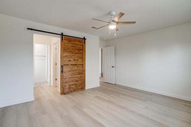 spare room with visible vents, light wood-style flooring, a barn door, ceiling fan, and baseboards