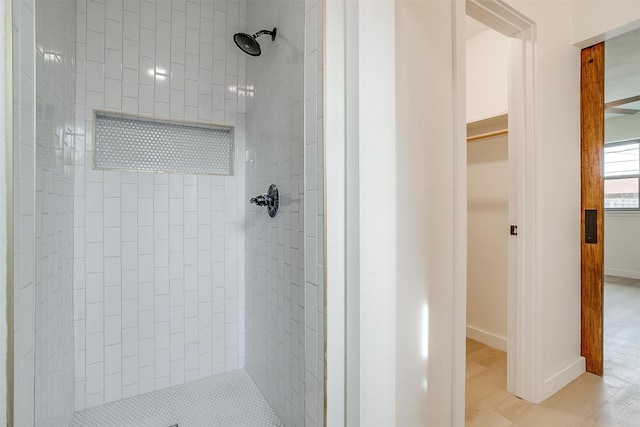 full bath with a spacious closet, wood finished floors, a tile shower, and baseboards