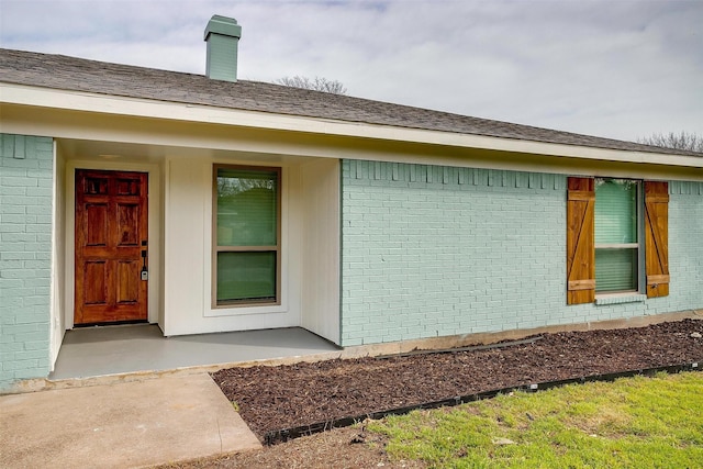 doorway to property with a shingled roof and brick siding