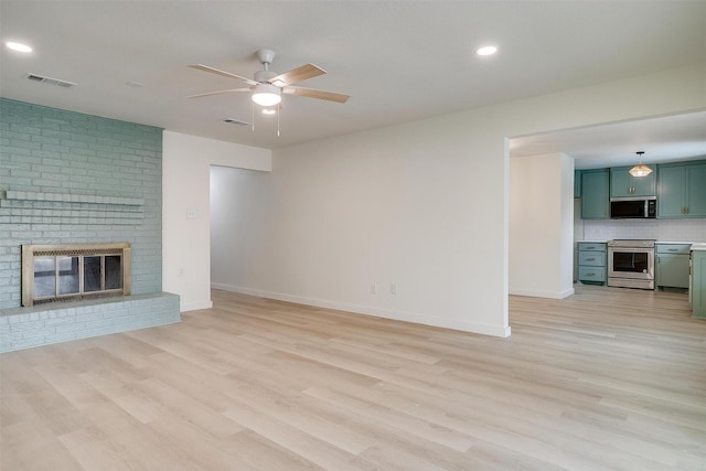 unfurnished living room with light wood-style flooring, a fireplace, visible vents, and ceiling fan