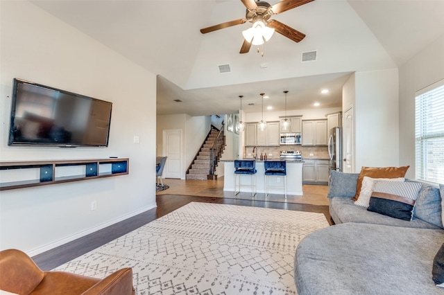 living room featuring visible vents, ceiling fan, light wood-style flooring, and stairs