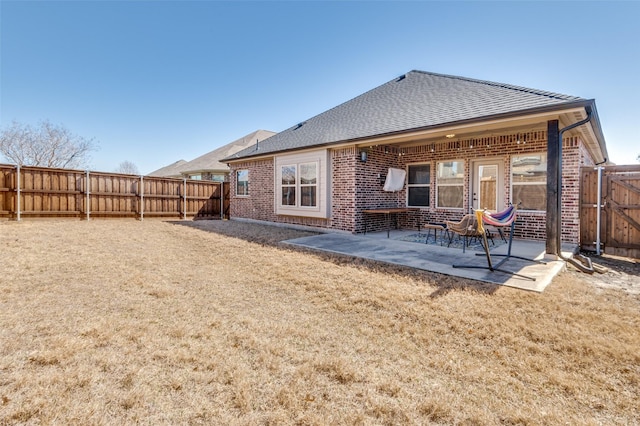 back of property with a yard, brick siding, a fenced backyard, and a patio area