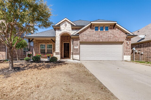 french provincial home with driveway, roof with shingles, brick siding, and a garage