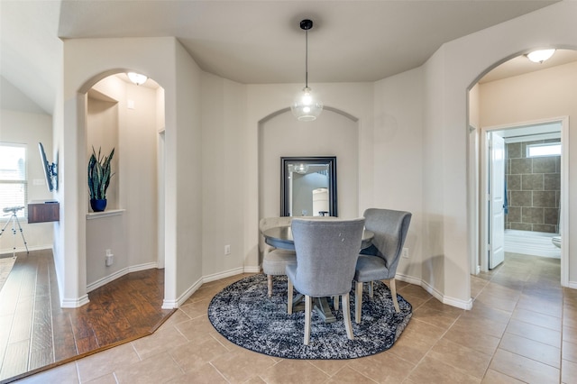 dining room featuring arched walkways, light tile patterned floors, and baseboards