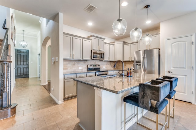 kitchen with visible vents, a sink, stainless steel appliances, a breakfast bar area, and stone counters