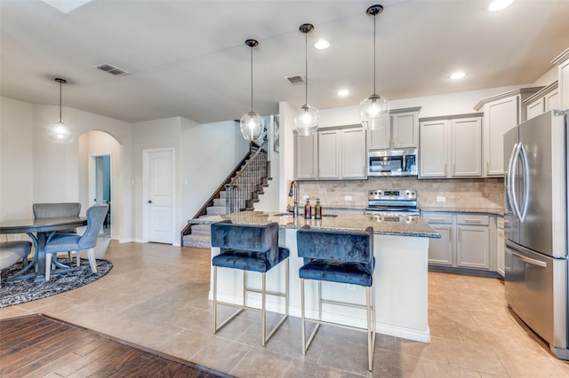 kitchen featuring a kitchen bar, stone counters, decorative backsplash, appliances with stainless steel finishes, and arched walkways