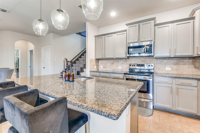 kitchen featuring gray cabinets, a sink, arched walkways, appliances with stainless steel finishes, and decorative backsplash