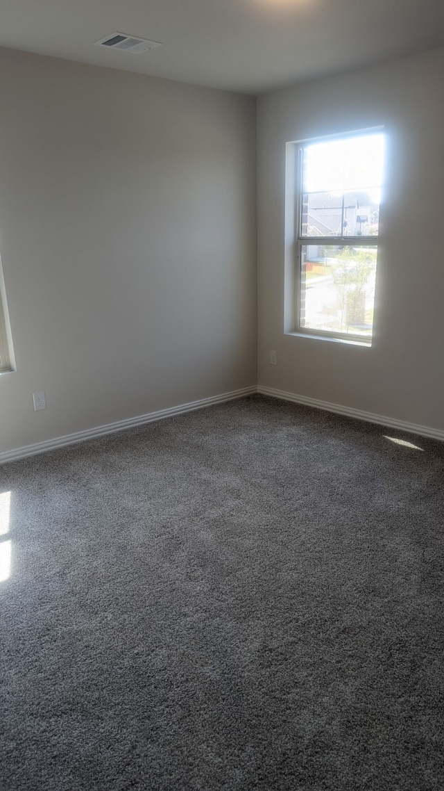 empty room with dark colored carpet, visible vents, and baseboards