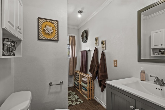 bathroom featuring toilet, wood finished floors, vanity, baseboards, and crown molding