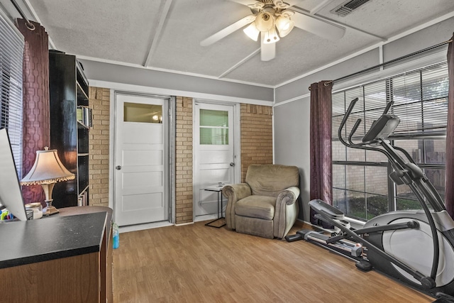 exercise area featuring ceiling fan, a textured ceiling, brick wall, visible vents, and light wood-style floors