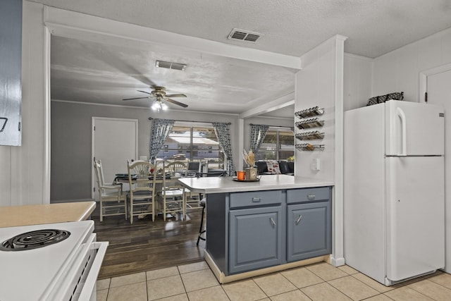 kitchen with light tile patterned floors, a textured ceiling, visible vents, light countertops, and freestanding refrigerator