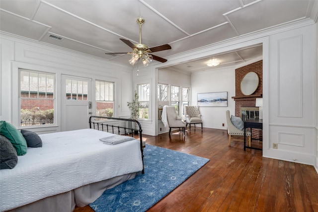 bedroom with visible vents, wood-type flooring, crown molding, a fireplace, and a decorative wall