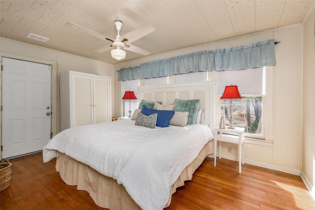 bedroom with a ceiling fan, visible vents, baseboards, and hardwood / wood-style flooring