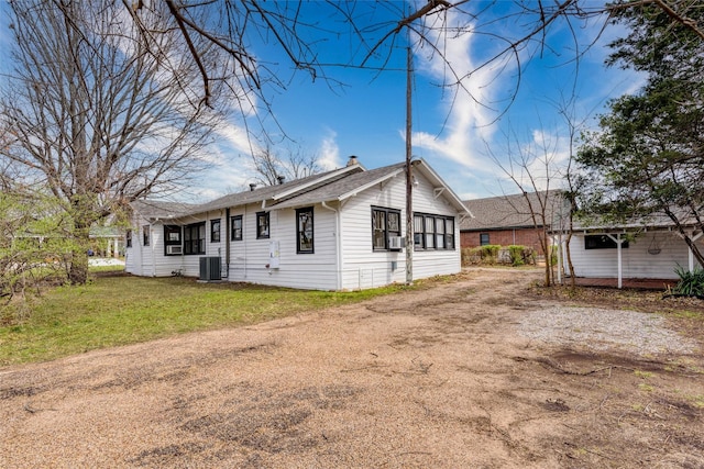 rear view of property featuring dirt driveway, central AC, a lawn, and cooling unit