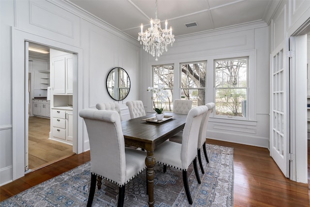 dining space featuring dark wood finished floors, visible vents, a decorative wall, ornamental molding, and a chandelier