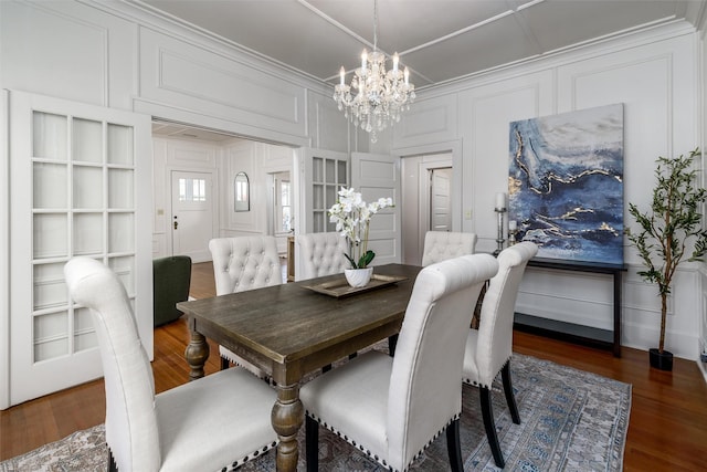 dining room with dark wood-style floors, a chandelier, crown molding, and a decorative wall