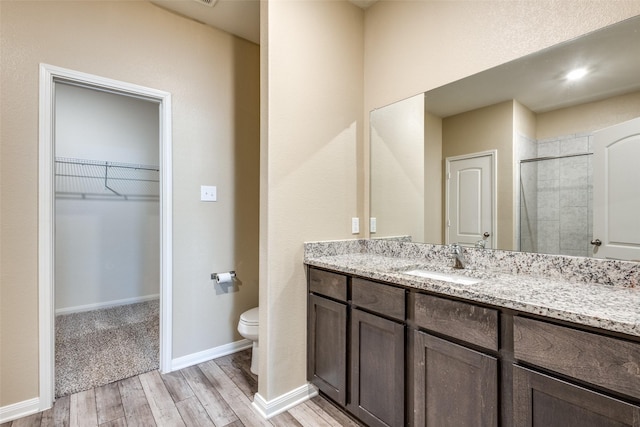 full bathroom featuring a walk in closet, toilet, vanity, wood finished floors, and baseboards