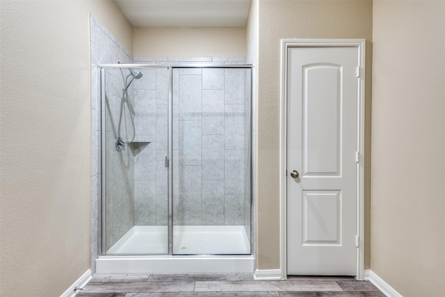 bathroom featuring wood finished floors, a shower stall, and baseboards